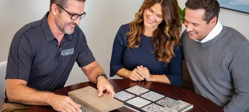 A premier garage consultant smiling and leaning over samples with two clients