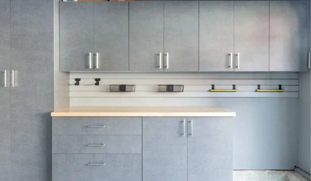 Light gray garage storage cabinet with wooden countertop and white slatwall storage system